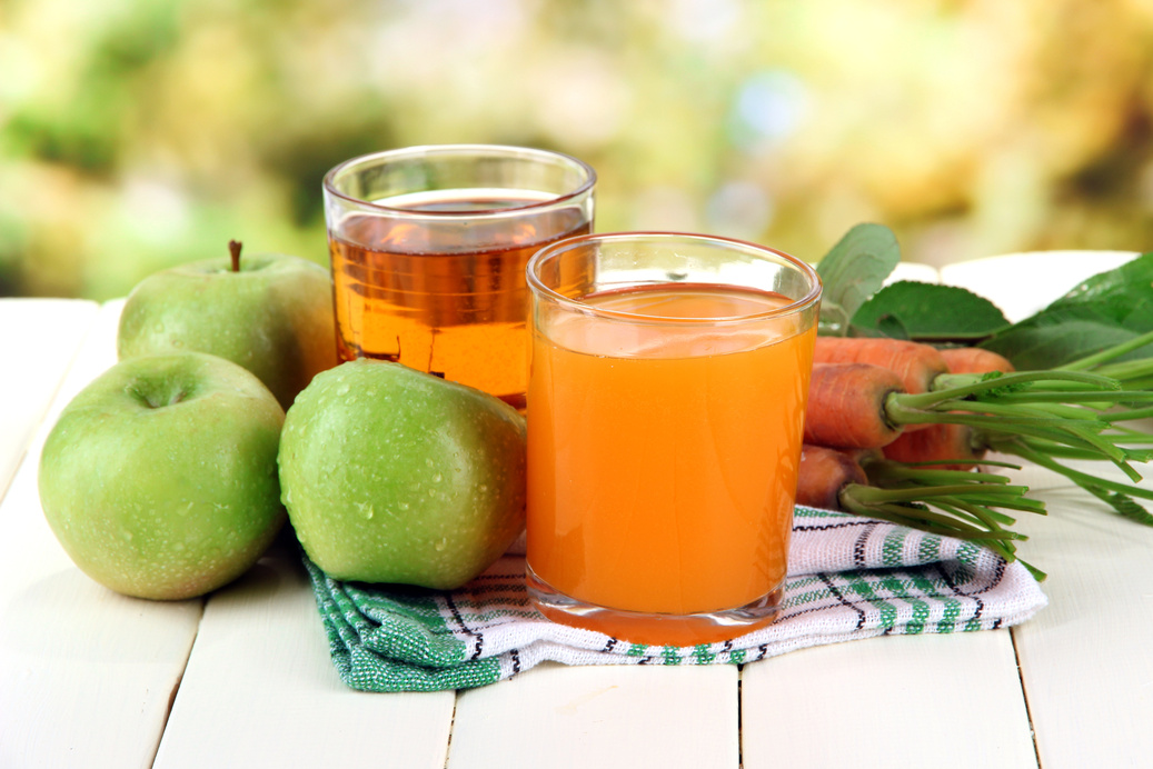 Glasses of Juice, Apples and Carrots on White Wooden Table, on Green Background